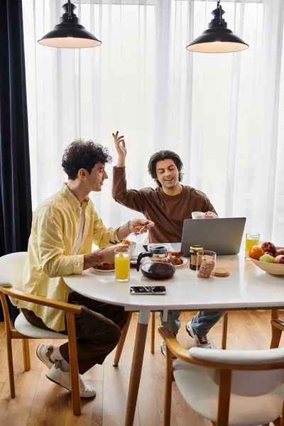 A couple laughs and shares a meal while working on a laptop in their cozy apartment. — Stock Photo