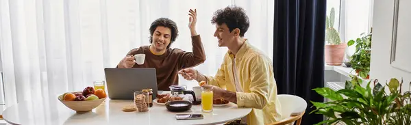 Two men share a joyful breakfast while working on a laptop in their contemporary home, banner — Stock Photo