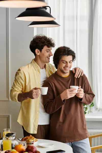 Zwei Männer genießen Kaffee und umarmen sich in ihrem stilvollen Zuhause, gebadet in warmem Sonnenlicht. — Stockfoto