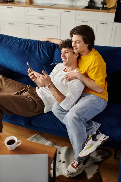 Two gay men relax on a plush couch, playfully engaging with their phones while sharing laughter. — Stock Photo