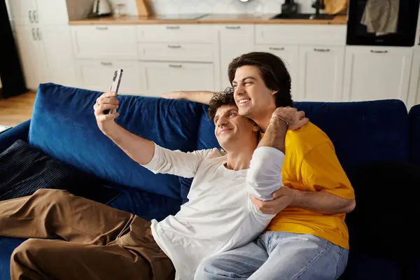 Two good looking men embrace joyfully while taking a selfie together in their stylish living space. — Stock Photo