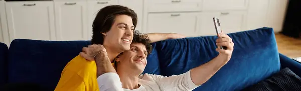 Dos hombres guapos comparten un momento tierno mientras se toman una selfie juntos en su apartamento moderno, pancarta - foto de stock