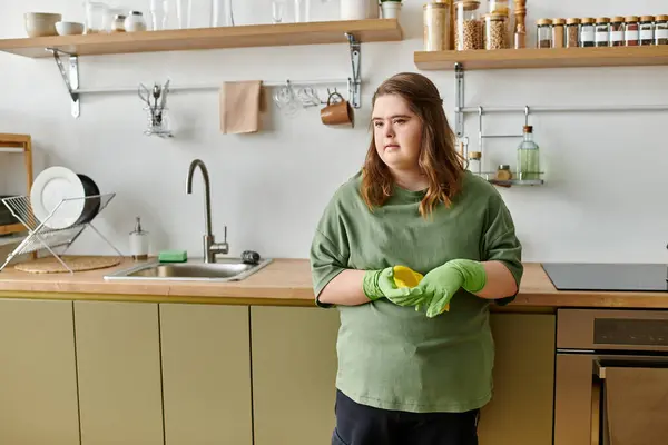 En una acogedora cocina, una joven con síndrome de Down está de pie con confianza, lista para asumir tareas. - foto de stock