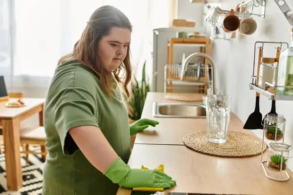 Em uma cozinha aconchegante, uma jovem com síndrome de Down limpa alegremente, mostrando sua independência. — Fotografia de Stock