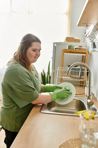 Hell und einladend spült eine junge Frau mit Down-Syndrom fröhlich Geschirr in ihrer gemütlichen Küche. — Stockfoto