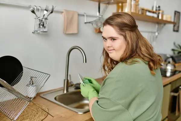 Uma jovem com síndrome de Down lava com confiança pratos em sua cozinha acolhedora. — Fotografia de Stock