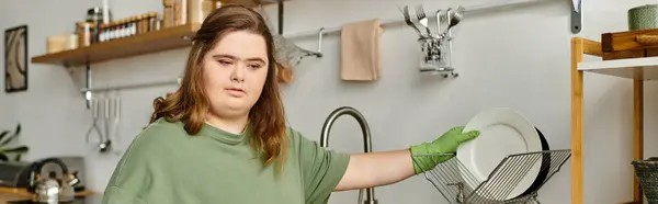 Una joven con síndrome de Down limpia platos en una cocina acogedora, irradiando confianza y comodidad. - foto de stock