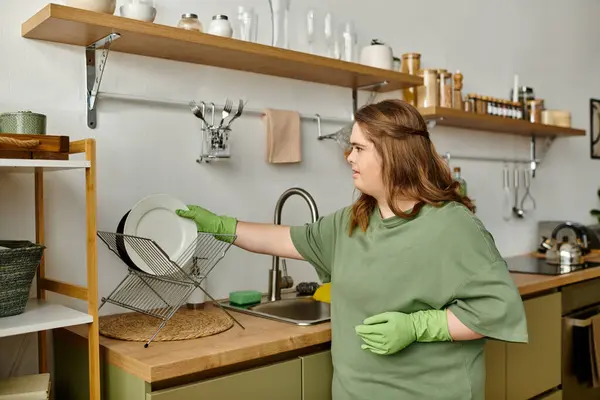 In a cozy kitchen, a young woman skillfully arranges dishes in vibrant green gloves. — Stock Photo