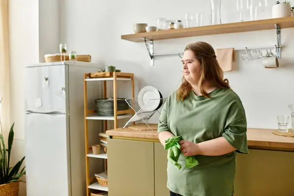Una joven con síndrome de Down abraza su acogedora cocina, sosteniendo un paño verde y sonriendo. - foto de stock
