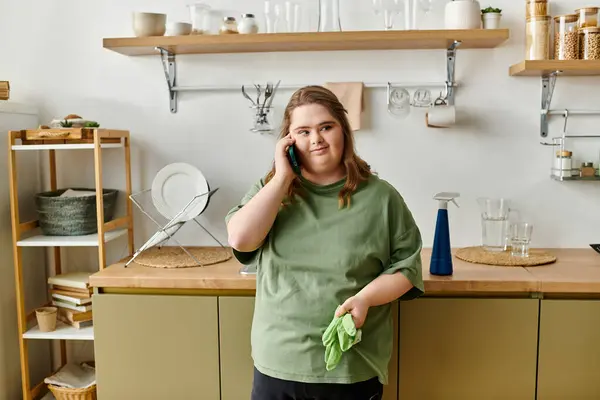 A young woman with Down syndrome talks on the phone in her cozy, decorated kitchen. — Stock Photo