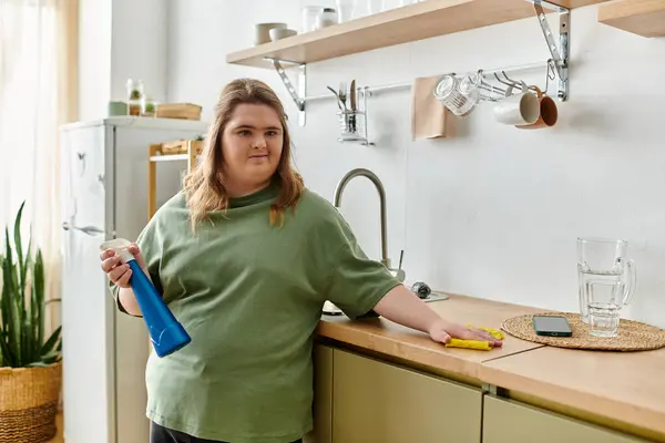A young woman with Down syndrome confidently cleans her cozy kitchen, radiating joy. — Stock Photo