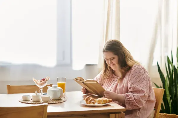 Young woman with Down syndrome relaxes at home, savoring a book and delicious pastries with warmth. — Stock Photo