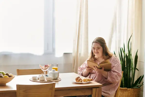 A young woman with Down syndrome enjoys reading and sweet treats in her cozy home. — Stock Photo