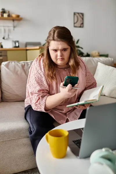 Una joven confiada lee y usa su teléfono en un ambiente hogareño brillante y acogedor. - foto de stock