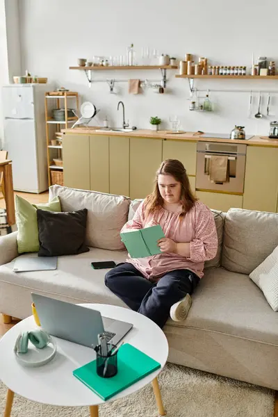 A young woman with Down syndrome reads comfortably on her couch in a warm home. — Stock Photo