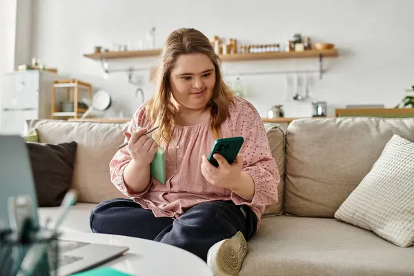 Confident young woman with Down syndrome relaxes at home, using her phone and notebook. — Stock Photo