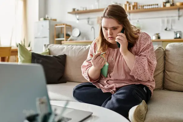 A young woman with Down syndrome sits comfortably on a couch at home, speaking on her phone. — Stock Photo