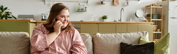 In a cozy home, a young woman with Down syndrome smiles and chats on the phone, feeling confident. — Stock Photo