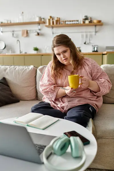 Pretty young woman with Down syndrome sits comfortably at home, enjoying her tea and a good book. — Stock Photo