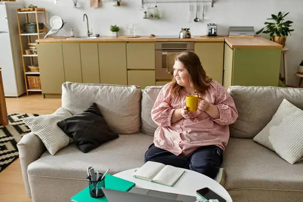 Young woman with Down syndrome relaxes on a couch with a warm cup and notebook at home. — Stock Photo