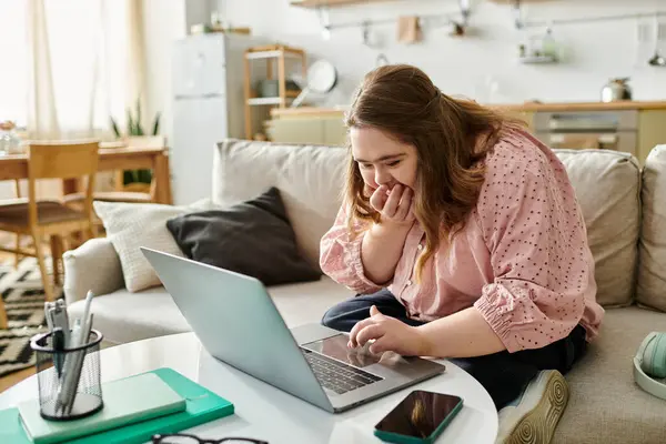 Young woman with Down syndrome smiles while using her laptop in a cozy home. — Stock Photo