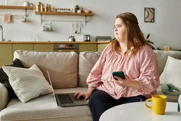 Young woman comfortably relaxes at home, using her laptop and phone, embracing her confidence. — Stock Photo