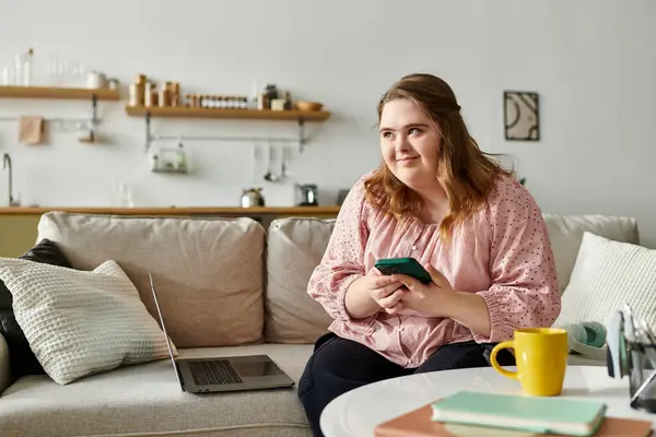 A young woman with Down syndrome relaxes at home, confidently engaging with her phone. — Stock Photo