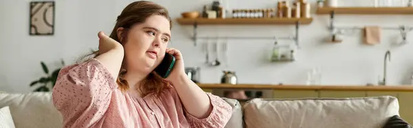 Una joven con síndrome de Down habla con confianza por teléfono en su acogedora casa. - foto de stock