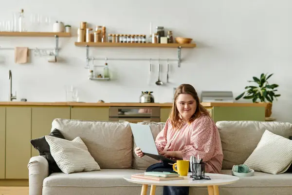 A young pretty woman with Down syndrome relaxes comfortably at home, smiling while using a device. — Stock Photo