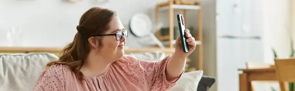 A young pretty woman with Down syndrome relaxes at home while watching her favorite show with joy. — Stock Photo