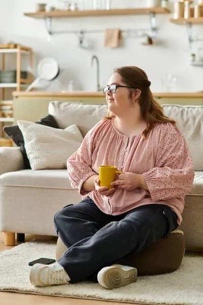 A confident young woman with Down syndrome sips from a yellow mug in a cozy living room. — Stock Photo
