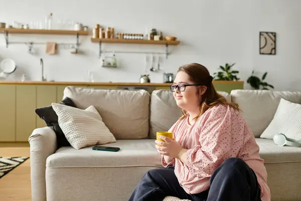 A pretty young woman with Down syndrome sits comfortably on the sofa, sipping tea and relaxing. — Stock Photo