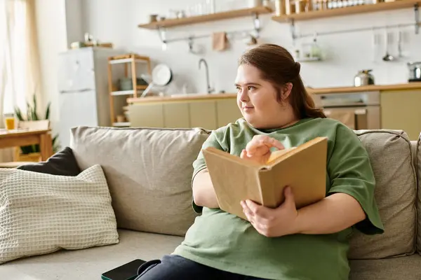 A young woman with Down syndrome enjoys a cozy moment at home, reading with confidence. — Stock Photo
