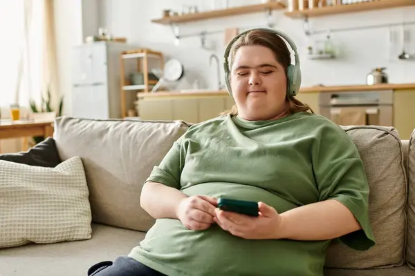 In a cozy living room, a young woman with Down syndrome joyfully listens to music with headphones. — Stock Photo
