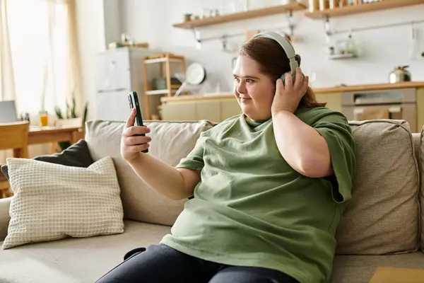 A young woman with Down syndrome relaxes at home, smiling and listening to music on her phone. — Stock Photo