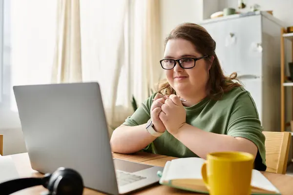 Woman with Down syndrome sits comfortably at home, focused on her laptop while thinking deeply. — Stock Photo
