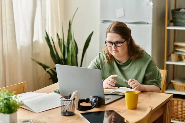 Una joven con síndrome de Down se centra en sus tareas creativas en una mesa acogedora, sintiéndose segura. - foto de stock