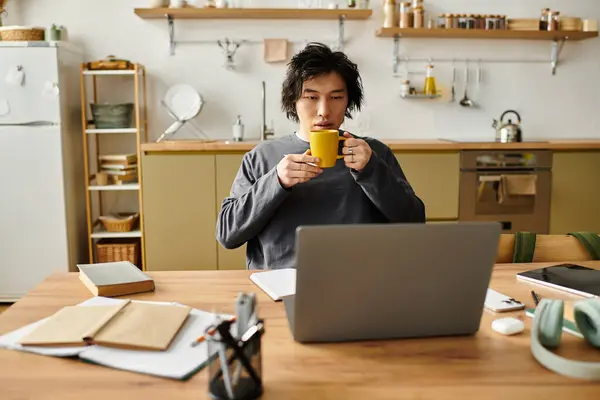 Young asian man studies diligently at home, sipping coffee and using a laptop for online classes. — Stock Photo