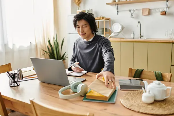 Young man is focused on his studies using a laptop at his home workspace, surrounded by books. — Stock Photo