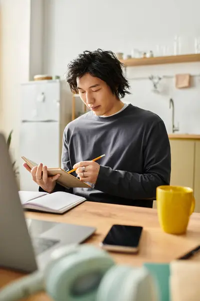 A young Asian man is dedicated to studying from home, taking notes and focusing on his tasks — Stock Photo