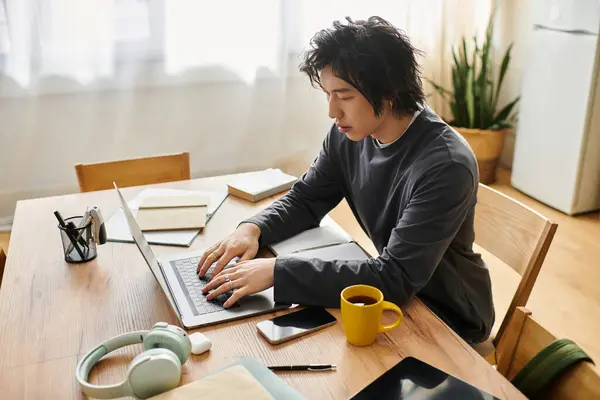 A handsome young man focuses on his laptop while studying at home, surrounded by books. — Stock Photo
