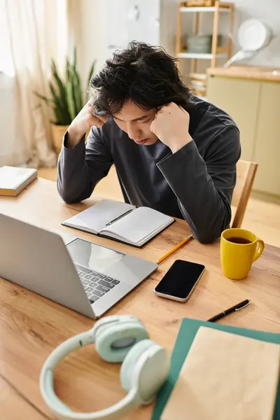 A handsome young Asian student studies intently at his desk with a laptop, notebook, and coffee. — Stock Photo