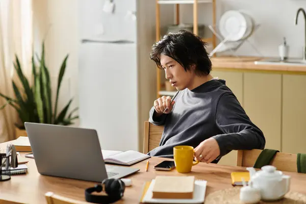 A sincere young man concentrates on his studies while seated at a wooden table with a laptop. — Stock Photo