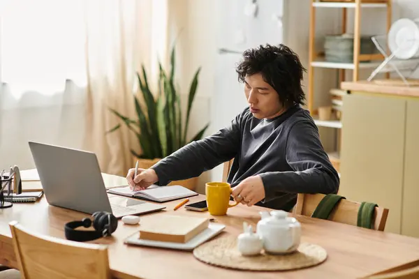 A handsome young man diligently studies online from his home while seated at a wooden table. — Stock Photo