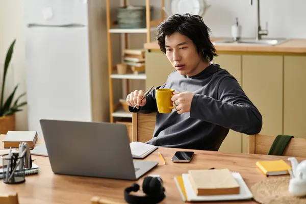 A handsome young man studies online from his home, sipping coffee while focused on his laptop. — Stock Photo