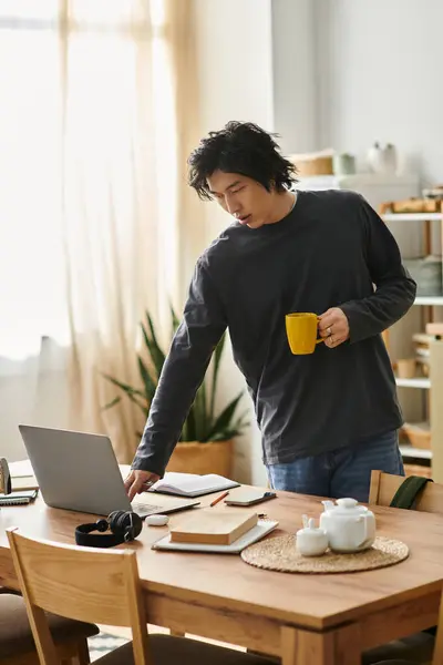 A handsome young man studies from home, using his laptop while enjoying a beverage. — Stock Photo