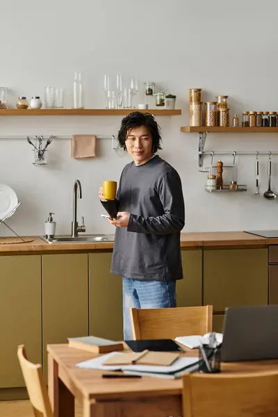 Un estudiante motivado se centra en el aprendizaje en línea en casa, disfrutando del café en una acogedora cocina. - foto de stock