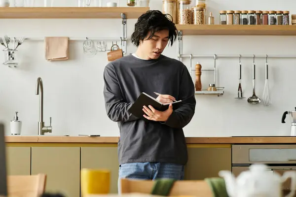 A handsome young man diligently taking notes while studying online in a cozy kitchen space. — Stock Photo
