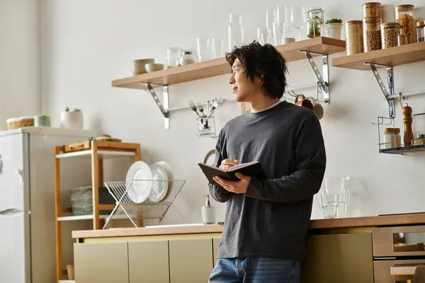A focused young man studies online at home while taking notes in his notebook. — Stock Photo