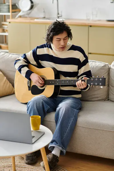 A young man with asian descent dedicates time to mastering acoustic guitar in a cozy living space. — Stock Photo